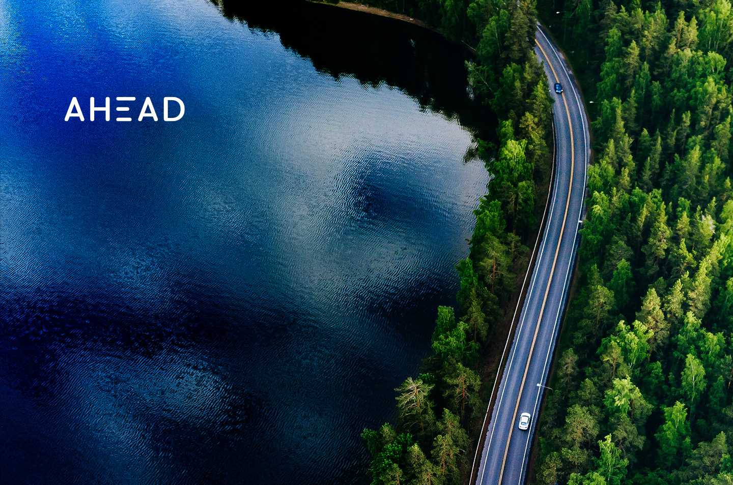 an arial view of a road cutting between a lake and a forest