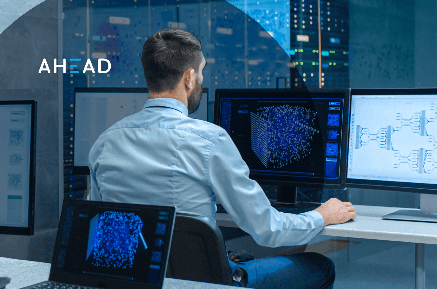 a man sitting at a desk in front of multiple computer monitors