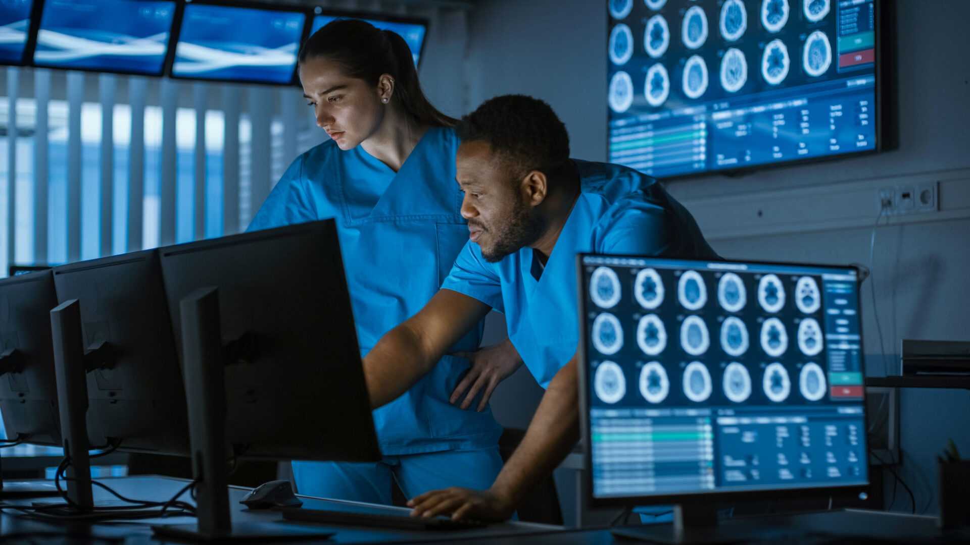 Two doctors facilitating and monitoring an MRI from a control room in a hospital