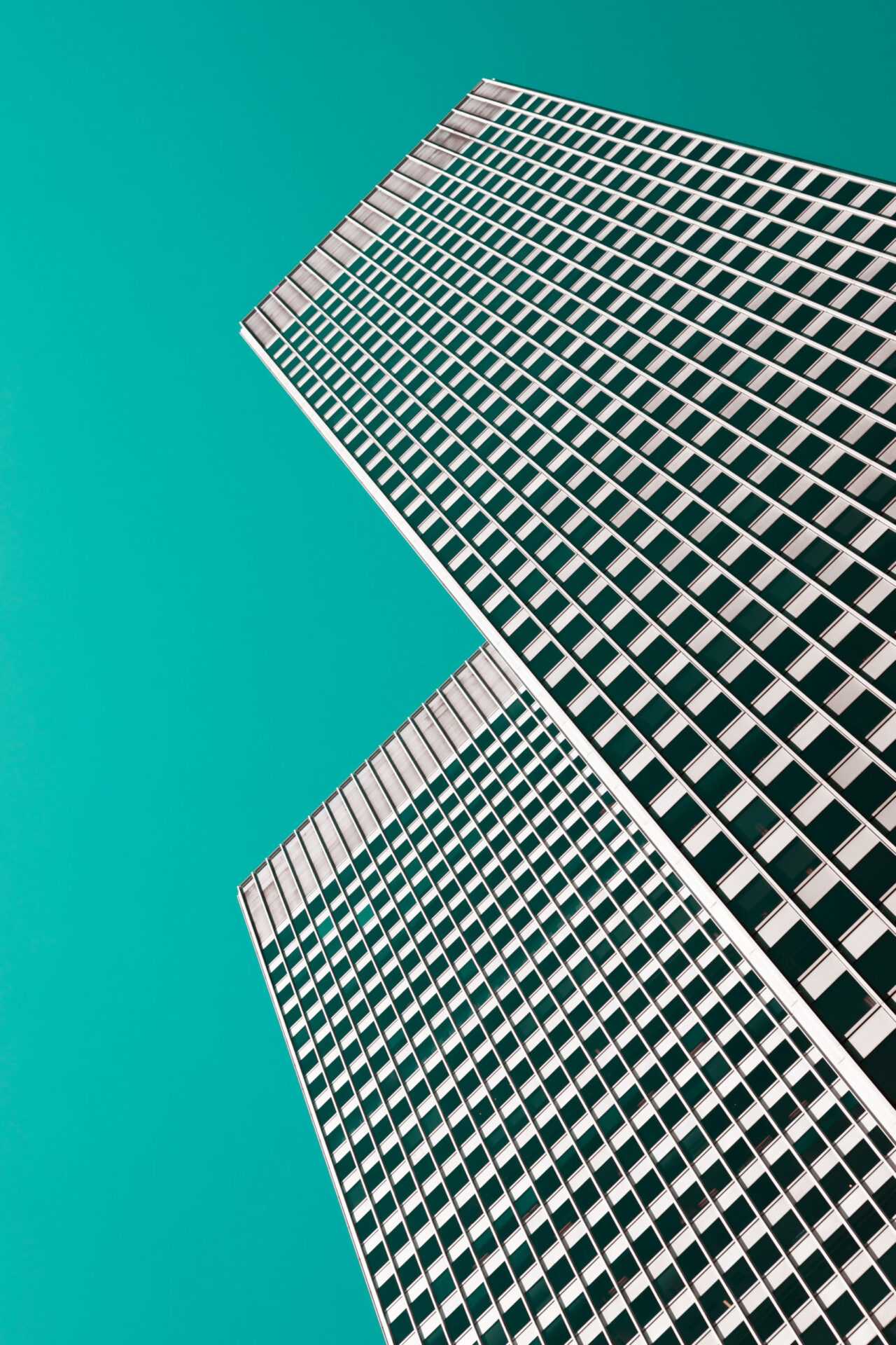 Two tall buildings on a teal background viewed from below